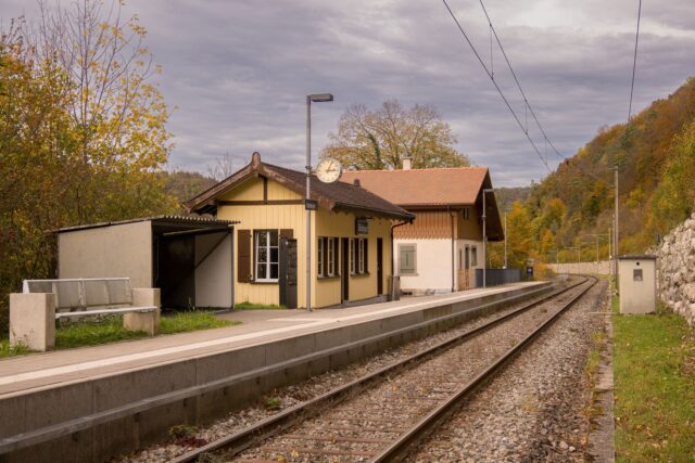 Mică gară rurală la poalele munților, toamna, cu un tren regional oprit la peron
