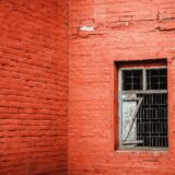 Colț de cameră într-o casă veche, cu pete de mucegai lângă fereastră și tencuială scorojită